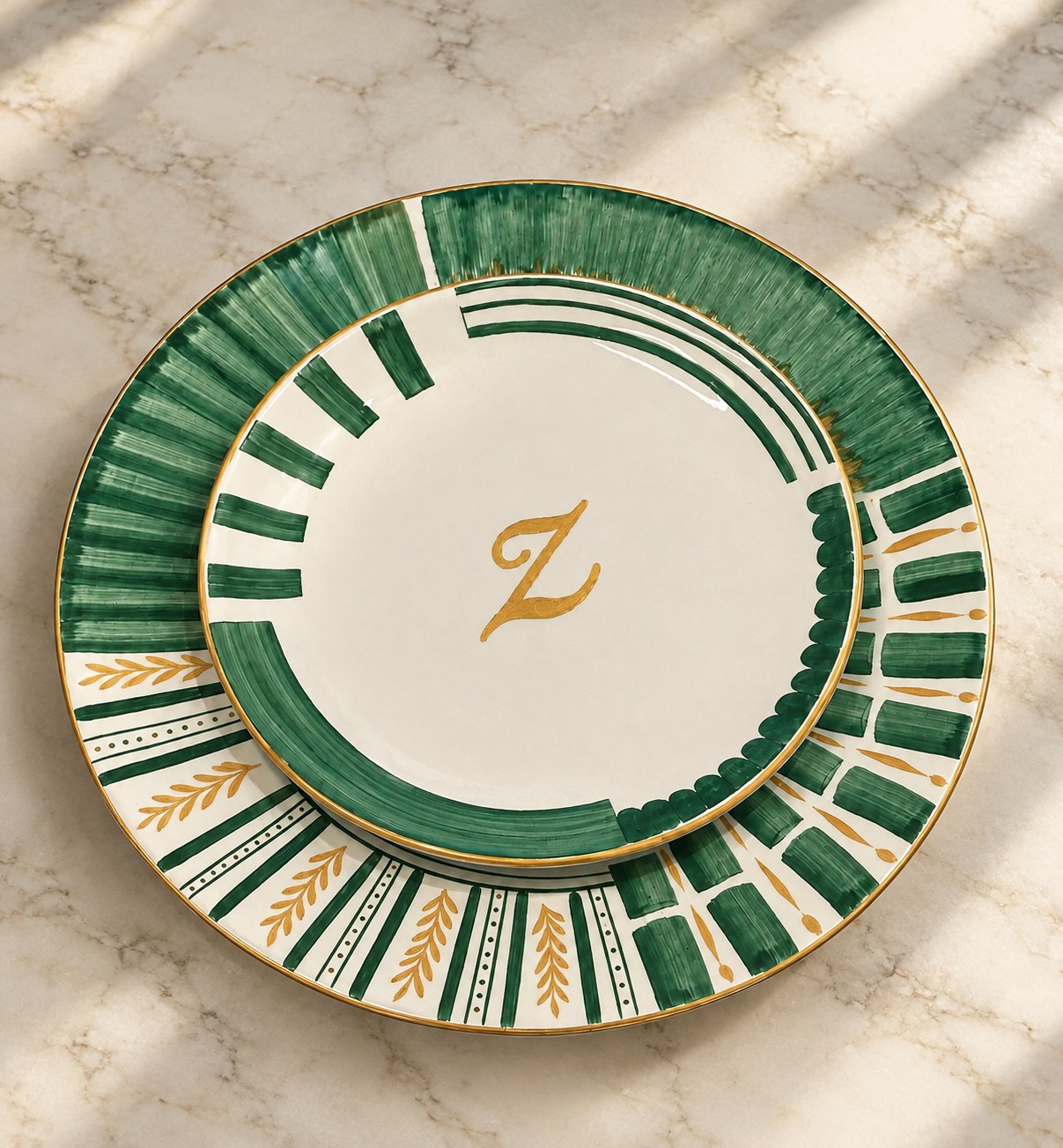 Two stacked porcelain plates with brushed green bands, gold leaves and a hand-lettered gold initial, on marble