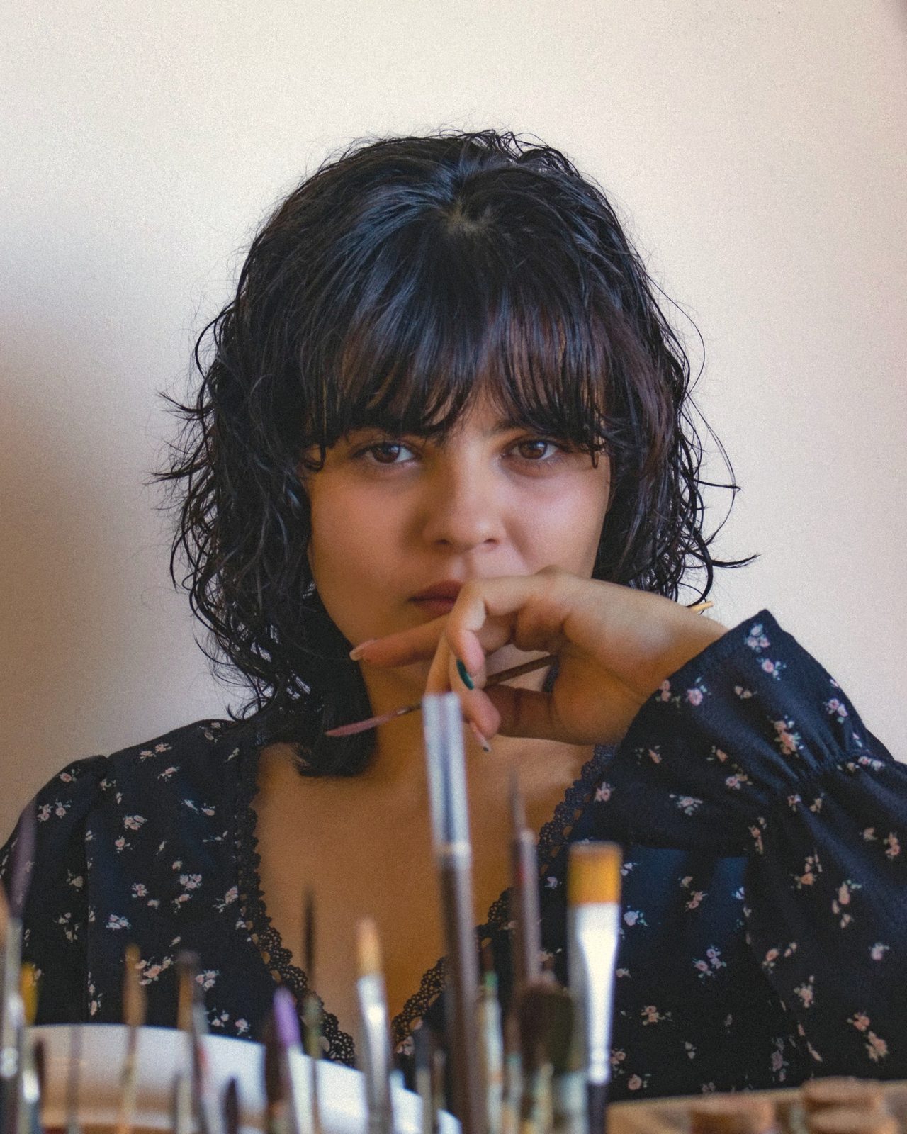 Pia Maria Nehme, resting her chin on her hand and holding a fine brush, with brushes in the foreground