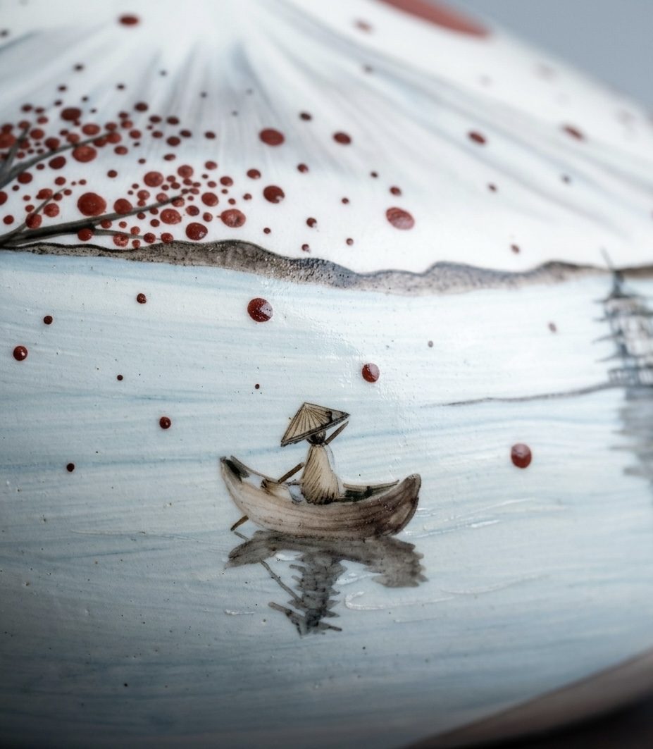 Detail of a boatman in a conical hat rowing across pale blue water under falling red leaves