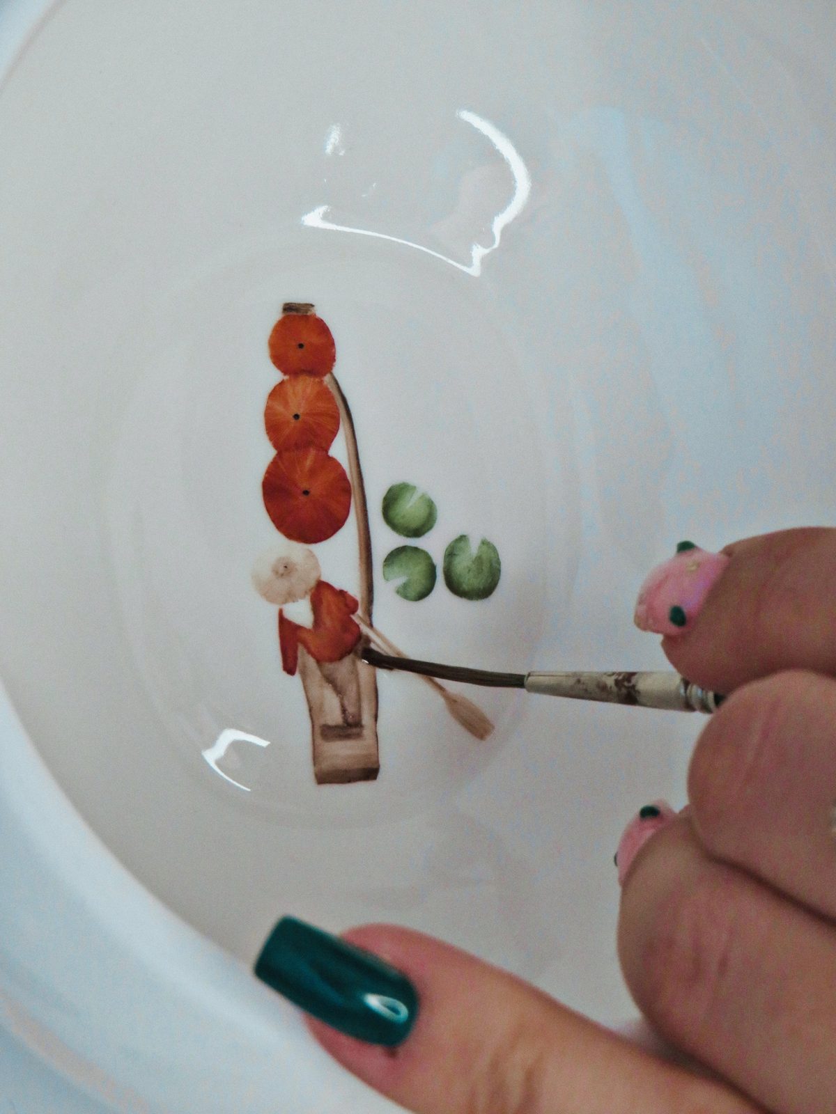 A hand painting a small figure inside a white porcelain bowl